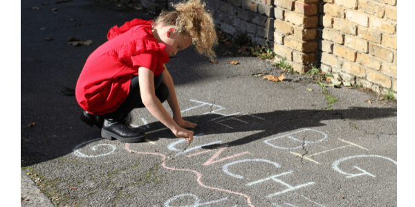 Child writing The Big Lunch on pavement