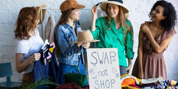 Four women trying on clothes at a community swap shop with text: 'Swap not shop'