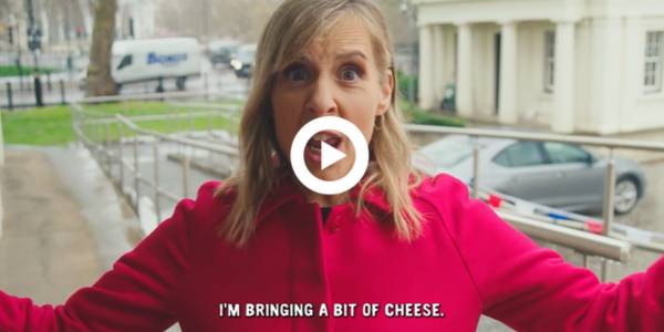Film still showing Mel Giedroyc with arms outstretched with text: 'I'm brining a bit of cheese' and play button