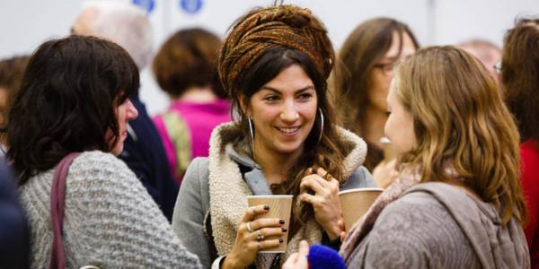 Women at a community event talking and holding hot drinks