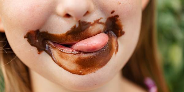 Little girl licking her mouth with chocolate all around it 