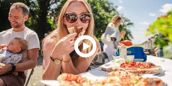 Woman eating pizza at a Big Lunch street party with play button 