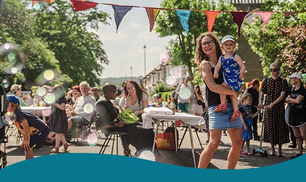 Woman holding toddler at a street party with community and tables and bunting 