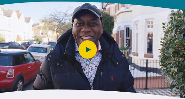 Ainsley Harriet smiling at camera in a street with play button