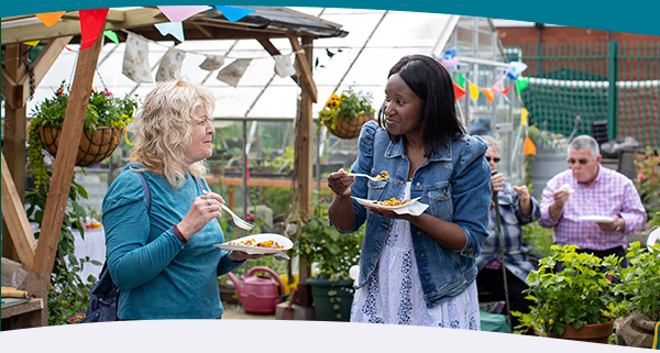Two women eating and chatting in a community garden at a Big Lunch