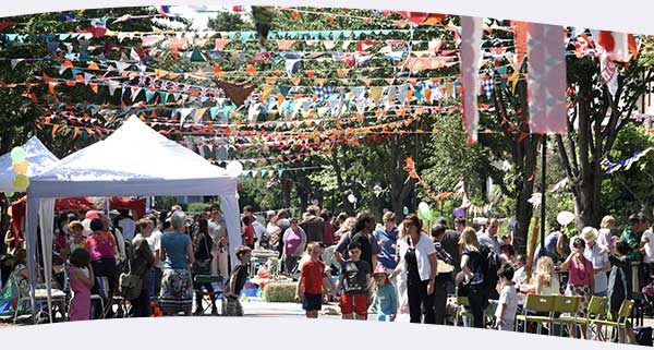 Big Lunch street party with crowds of people and colourful bunting, gazeebos and chairs