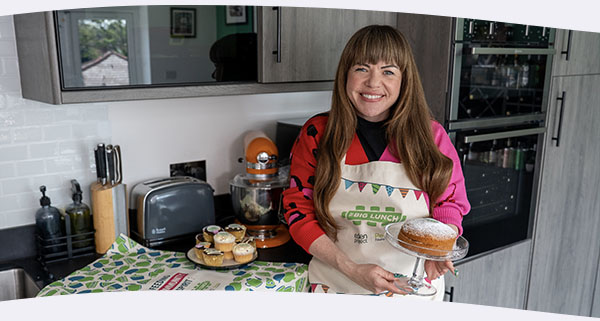 Briony May smiling with a sponge cake in hand in her kitchen