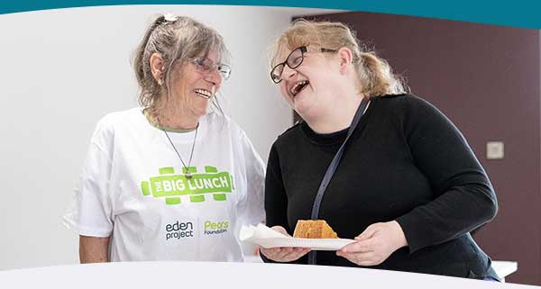 Two women laughing at a Big Lunch event with cake in hand