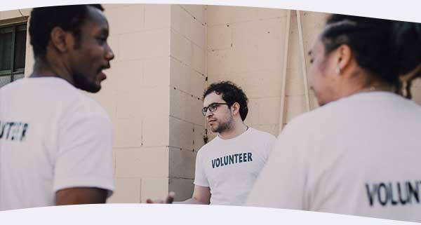 Three men in Volunteering t-shirts outside talking